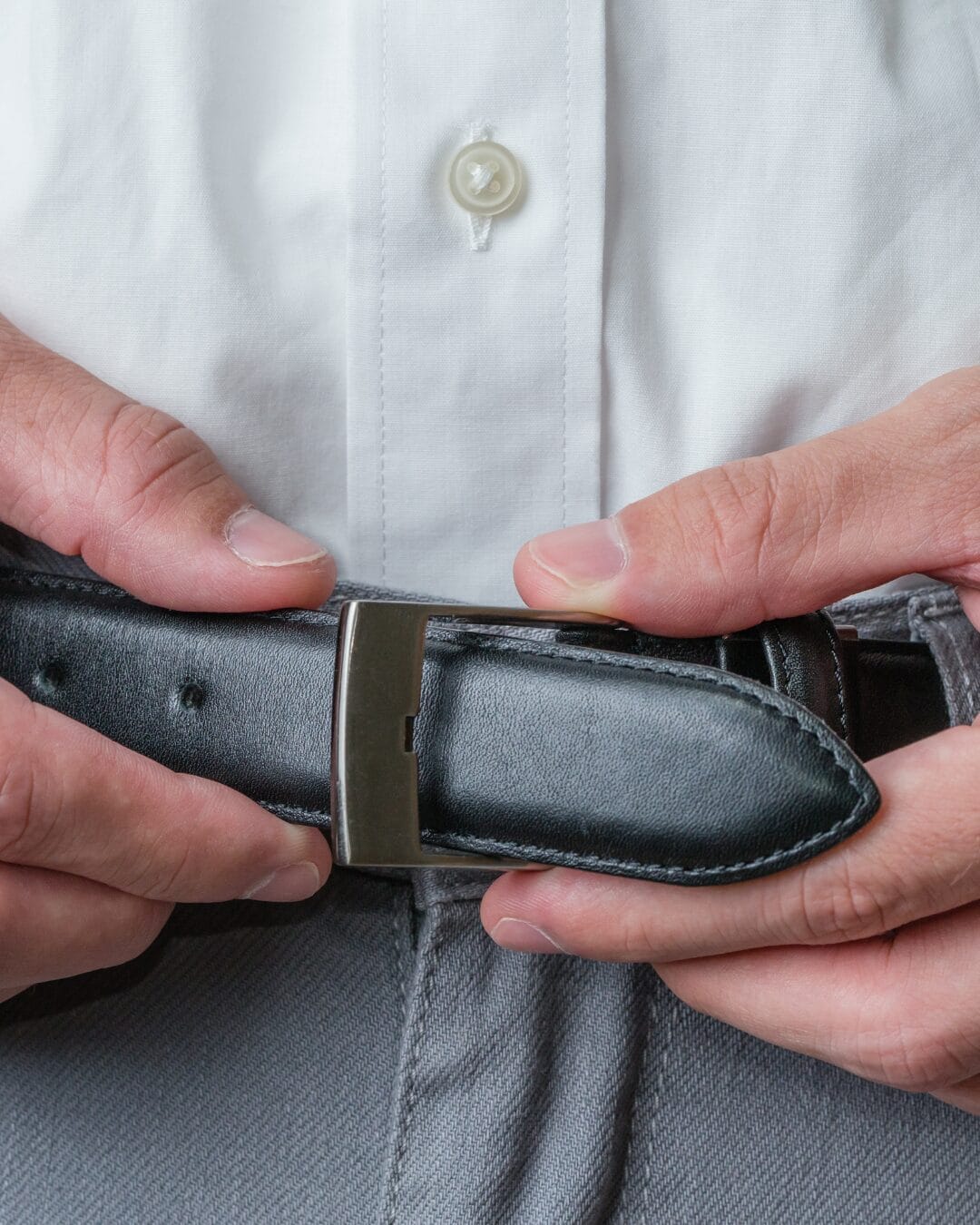 Close-up of a man fastening a black leather belt for Male Enhancement treatment