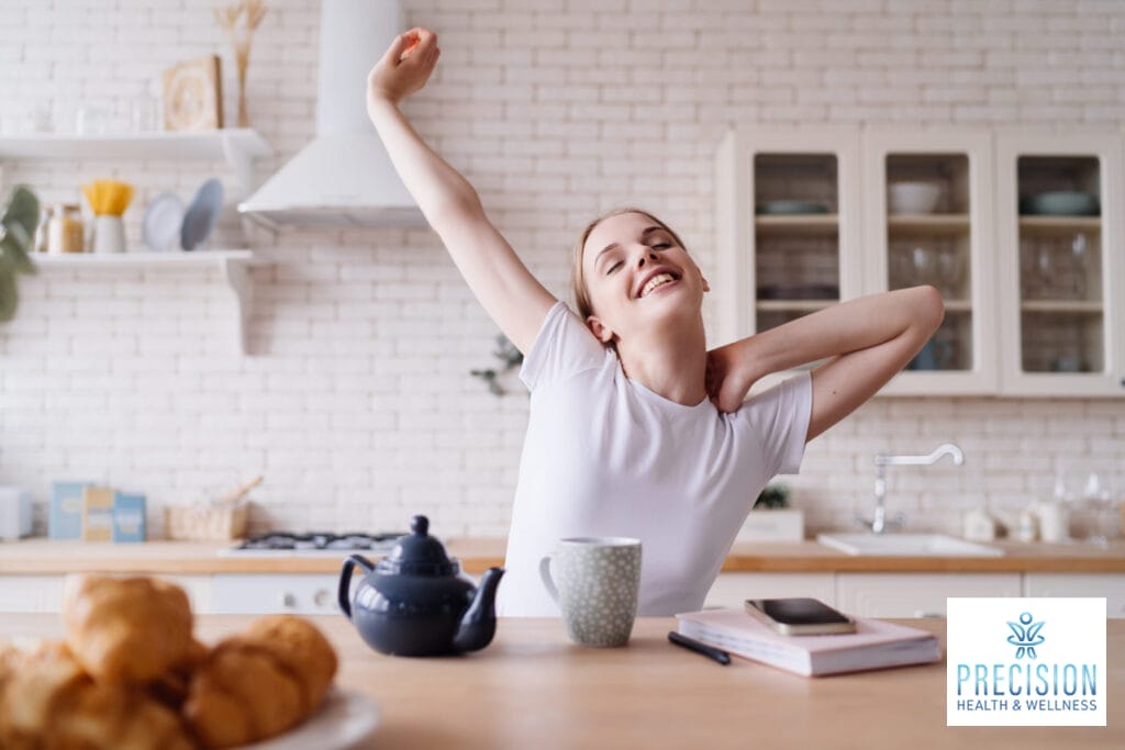 Happy woman stretching in a bright kitchen, representing increased energy and vitality from hormone optimization.