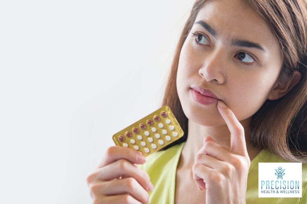 Thoughtful woman holding birth control pills, considering options for balancing hormones through optimization treatments.