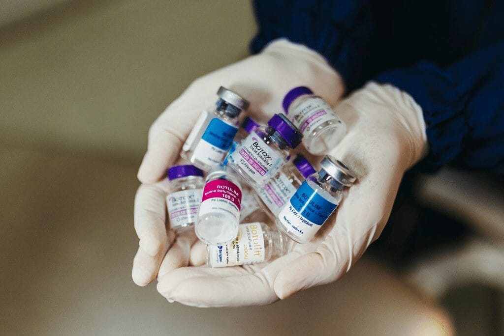 Gloved hands holding various cosmetic injectable bottles
